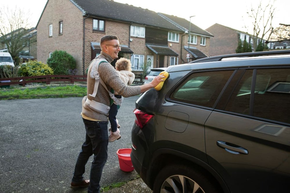 A father washing the family car on the driveway outside their home